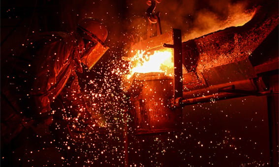 Foundry and industrial steel production. Worker standing by furnace with hot molten iron and sparks flying